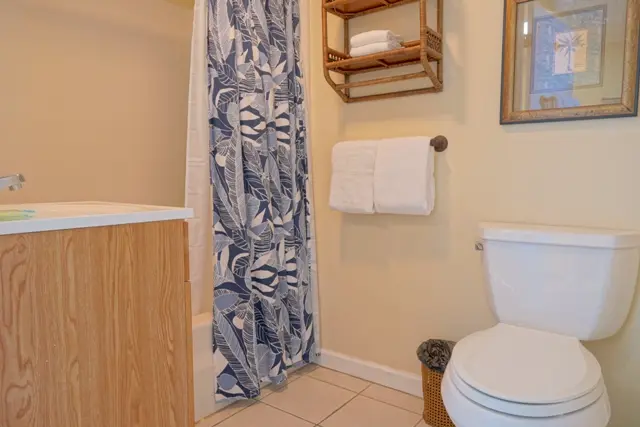A bathroom with a leaf-print shower curtain, a towel rack with white towels and a toilet