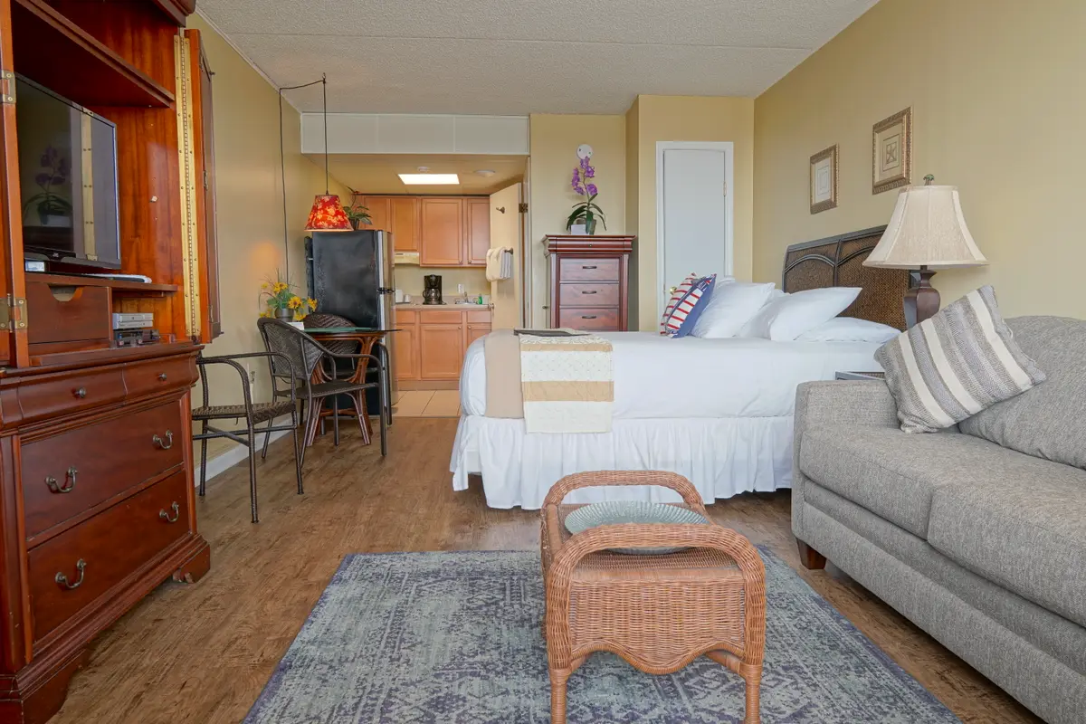 A studio with a king bed, a gray sofa bed, a wood entertainment cabinet and a small dining table by the kitchenette