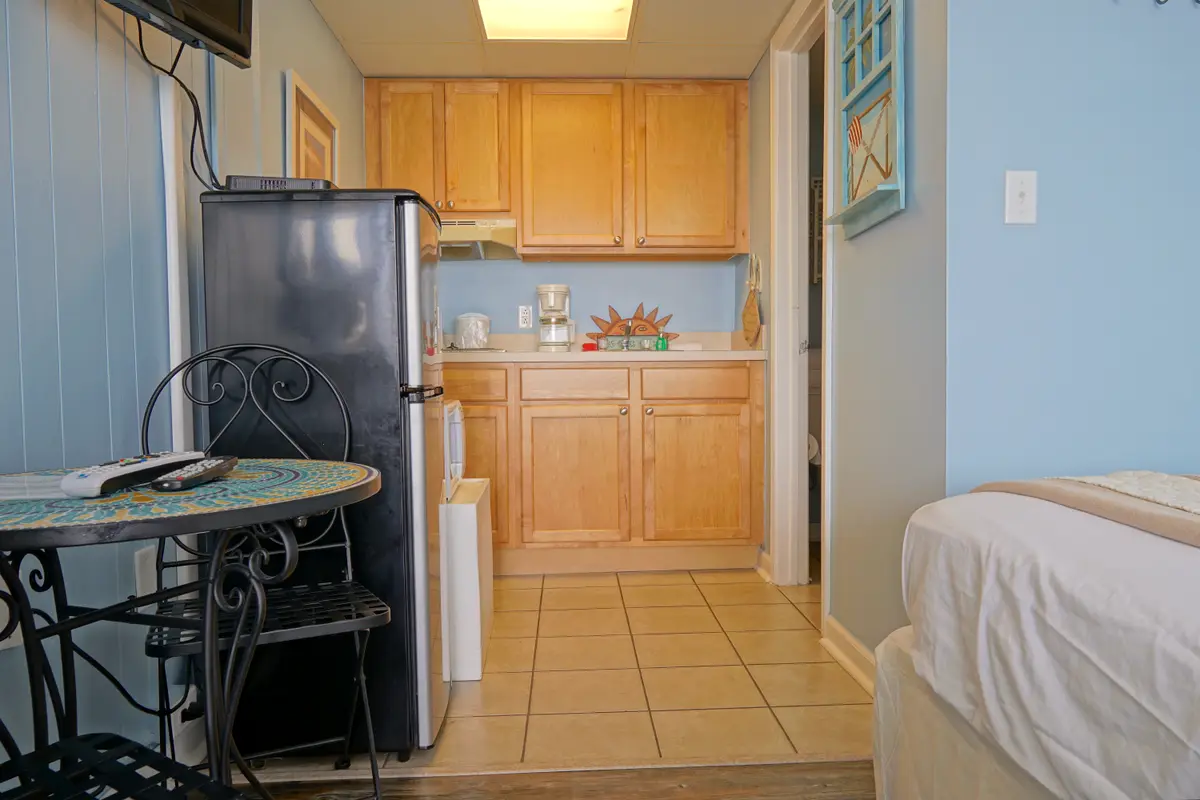 A round mosaic bistro table and chairs beside a stainless refrigerator and the kitchenette cabinets
