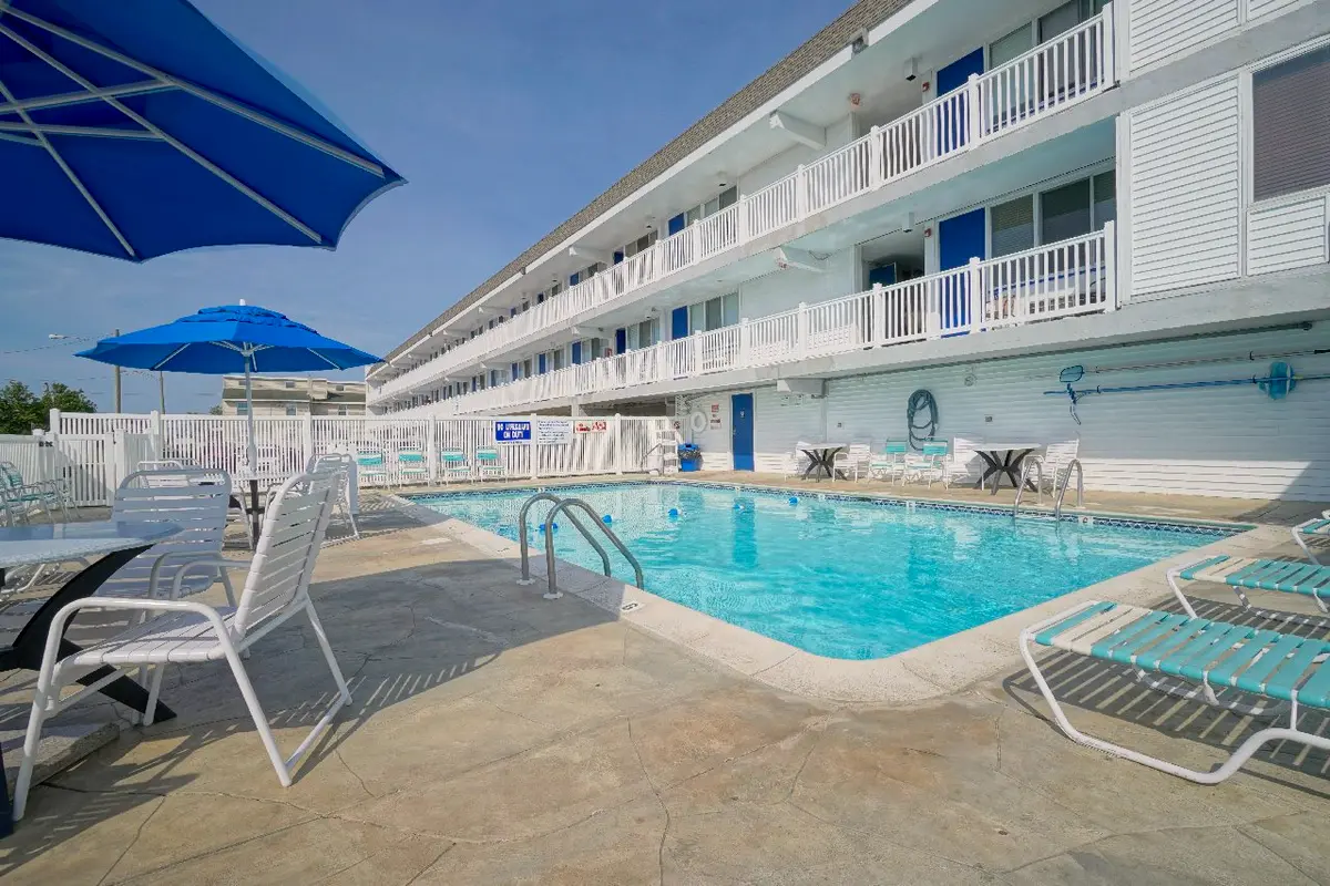 The outdoor pool with lounge chairs and blue umbrellas, surrounded by the building’s white railed balconies